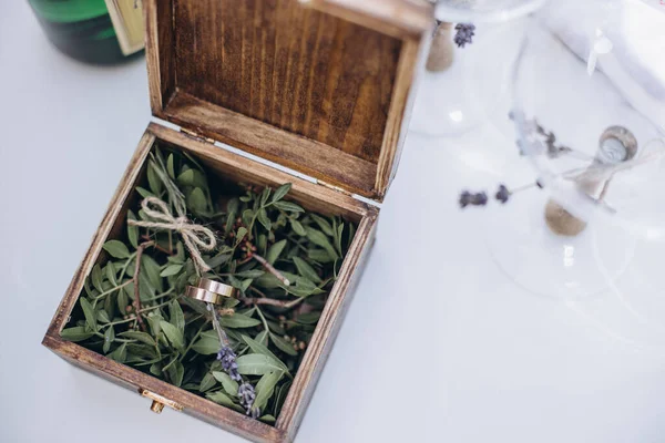 Zlaté snubní prsteny leží na provazech v dřevěné krabici se zrcadlem, které stojí na trávě. — Stock fotografie