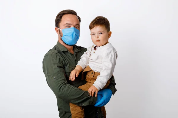 Genç babası ve küçük oğlu beyaz bir arka planda cerrahi maske takıyor.