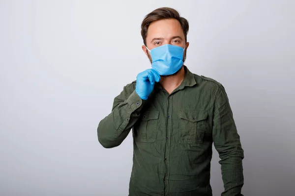 Yüzünde tıbbi bir maskeyle beyaz arka planda genç bir adam Coronavirus ve diğer hastalıklara karşı koruyor.
