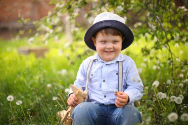 Güneşli bir günde, yaz parkında, çimlerin üzerinde tahta bir uçakla oynayan tatlı sarışın çocuk.