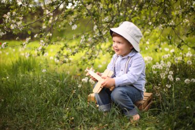 Güneşli bir günde, yaz parkında, çimlerin üzerinde tahta bir uçakla oynayan tatlı sarışın çocuk.