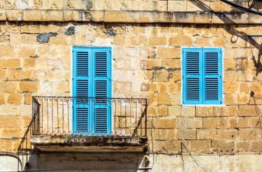 Cospicua, Malta 'da kireçtaşı duvarında açık mavi kepenkleri olan pencere ve balkon. Otantik Malta şehir sahnesi.