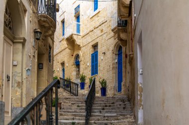 Birgu, Malta 'da dar ve büyüleyici bir cadde. Kireçtaşı binalar, lacivert kapılar, pencere panjurları ve duvarlar boyunca uzanan mavi kaplar..