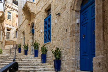 Birgu, Malta 'da dar ve büyüleyici bir cadde. Kireçtaşı binalar, lacivert kapılar, pencere panjurları ve duvarlar boyunca uzanan mavi kaplar..