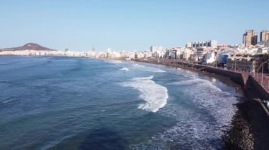 Las Canteras Sahili 'nin (Playa de Las Canteras (Las Palmas de Gran Canaria) insansız hava aracı görüntüleri), dalgalar, binalar ve sörfçüler de dahil olmak üzere güneşli havada çekilmiştir..