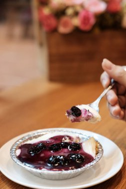 Yapay çiçek kokulu ahşap masa üzerinde yaban mersini peynir kek üzerine el 