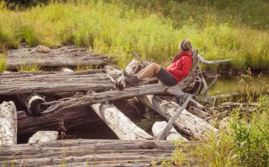 Yaz güneşinin tadını çıkaran bir kadın Gosford Dağı 'nda eski bir kütük köprüsünde oturuyor. Kanada' nın Quebec kenti ile Maine arasındaki sınırda.