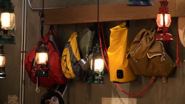 Цветные туристические рюкзаки висят вдоль стены в свете фонаря в стиле ретро — стоковое видео