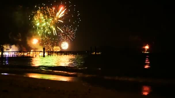 Bright golden fireworks explode in the night sky above the surface of the sea — Stock Video