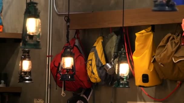 Colored tourist backpacks hanging along the wall in light of retro style lantern — Stock Video