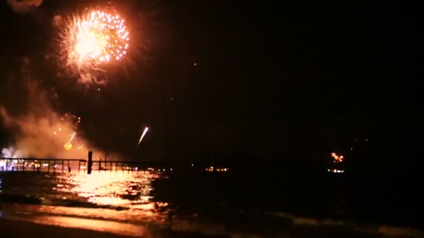 Bright golden fireworks explode in the night sky above the surface of the sea — Stock Video