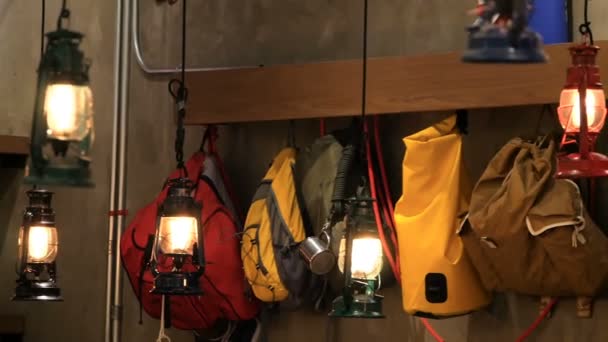 Colored tourist backpacks hanging along the wall in light of retro style lantern — Stock Video