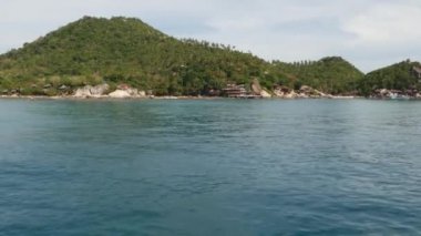 Yeşil tropikal cennet adasının yakınındaki sakin su. Tayland 'da bulutlu bir günde, yeşil tepe Tao Adası' ndaki dalış tesisi yakınlarında sakin bir deniz suyu. Tekneden görünüm.