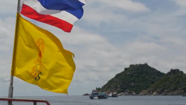 Barco flotando cerca de banderas tailandesas en día tropical soleado. Silueta de barco en el mar ondulante cerca de Tailandia y el rey de Tailandia banderas contra el cielo nublado una isla de paraíso koh Tao . — Vídeo de stock