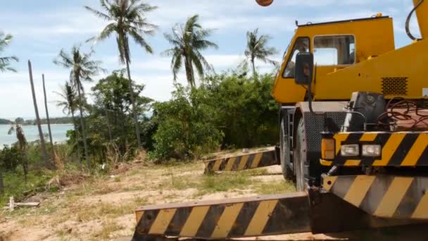 Máquinas de construção que trabalham na floresta tropical. Vista lateral do guindaste amarelo cortando árvores exóticas em trópicos. Perturbação do ecossistema e desflorestação . — Vídeo de Stock