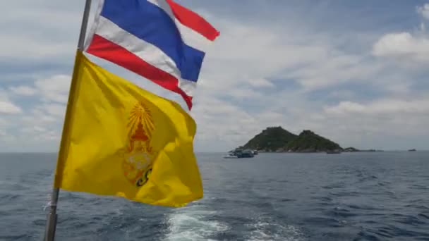 Barco flotando cerca de banderas tailandesas en día tropical soleado. Silueta de barco en el mar ondulante cerca de Tailandia y el rey de Tailandia banderas contra el cielo nublado una isla de paraíso koh Tao . — Vídeo de stock