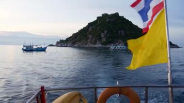 Akşamları Tayland bayraklarının yanında yüzen tekne. Tayland ve Tayland bayrakları yakınlarındaki dalgalı denizde yüzen isimsiz insanların silueti bulutlu günbatımına karşı.