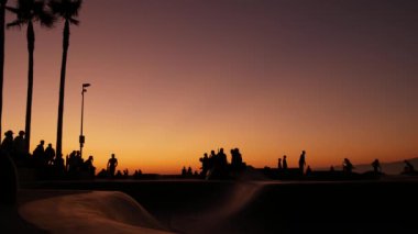 Yaz günbatımı arka planında, kaykayla gezen genç kaykaycı silueti. Venice Ocean Beach kaykay parkı, Los Angeles California. Kaykay rampasında gençler, ekstrem park. Bir grup genç..