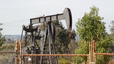 Endüstriyel şehir manzarası. La Brea Inglewood, Los Angeles 'ta. Çitin arkasında Jack 'i pompala. Sondaj kulesi ham petrol çıkarıyor. Çalışan pistonlu bir yağ makinası. Petrol ve doğalgaz endüstrisi