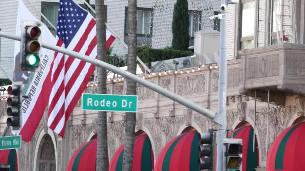 Världsberömda Rodeo Drive Street Road Logga in Beverly Hills mot amerikanska Unated States flagga. Los Angeles, Kalifornien, USA. Rik välbärgad livskonsumtion, lyxmärken, högklassigt butikskoncept. — Stockvideo