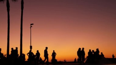 Yaz günbatımı arka planında, kaykayla gezen genç kaykaycı silueti. Venice Ocean Beach kaykay parkı, Los Angeles California. Kaykay rampasında gençler, ekstrem park. Bir grup genç..