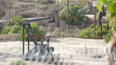 Endüstriyel şehir manzarası. La Brea Inglewood, Los Angeles 'ta. Çitin arkasında Jack 'i pompala. Sondaj kulesi ham petrol çıkarıyor. Çalışan pistonlu bir yağ makinası. Petrol ve doğalgaz endüstrisi