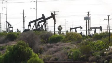 Endüstriyel şehir manzarası. La Brea Inglewood, Los Angeles 'ta. Çitin arkasında Jack 'i pompala. Sondaj kulesi ham petrol çıkarıyor. Çalışan pistonlu bir yağ makinası. Petrol ve doğalgaz endüstrisi