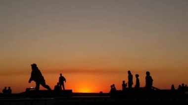 Yaz günbatımı arka planında, kaykayla gezen genç kaykaycı silueti. Venice Ocean Beach kaykay parkı, Los Angeles California. Kaykay rampasında gençler, ekstrem park. Bir grup genç..