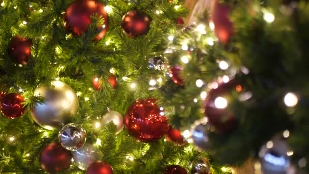 Primer plano del árbol de Navidad al aire libre decorado festivamente con bolas de color rojo brillante sobre el fondo borroso brillante hada. Luces de guirnalda desenfocadas, efecto Bokeh. Feliz Navidad y Felices Fiestas concepto. — Vídeos de Stock