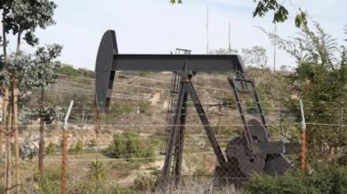 Endüstriyel şehir manzarası. La Brea Inglewood, Los Angeles 'ta. Çitin arkasında Jack 'i pompala. Sondaj kulesi ham petrol çıkarıyor. Çalışan pistonlu bir yağ makinası. Petrol ve doğalgaz endüstrisi