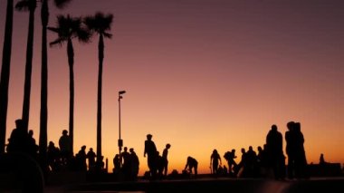 Yaz günbatımı arka planında, kaykayla gezen genç kaykaycı silueti. Venice Ocean Beach kaykay parkı, Los Angeles California. Kaykay rampasında gençler, ekstrem park. Bir grup genç..