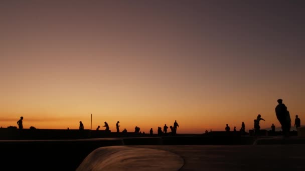 Σιλουέτα των νέων άλμα skateboarder ιππασία longboard, καλοκαίρι ηλιοβασίλεμα φόντο. Venice Ocean Beach skatepark, Λος Άντζελες Καλιφόρνια. Έφηβοι σε ράμπα σκέιτμπορντ, ακραίο πάρκο. Ομάδα εφήβων. — Αρχείο Βίντεο