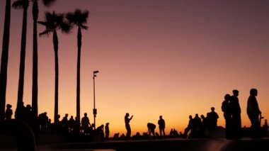 Yaz günbatımı arka planında, kaykayla gezen genç kaykaycı silueti. Venice Ocean Beach kaykay parkı, Los Angeles California. Kaykay rampasında gençler, ekstrem park. Bir grup genç..