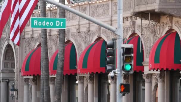 Wereldberoemde Rodeo Drive Street Road Sign in Beverly Hills tegen de Amerikaanse vlag van de Verenigde Staten. Los Angeles, Californië, Verenigde Staten. Rijk rijk leven consumentisme, luxe merken, high-class winkels concept. — Stockvideo