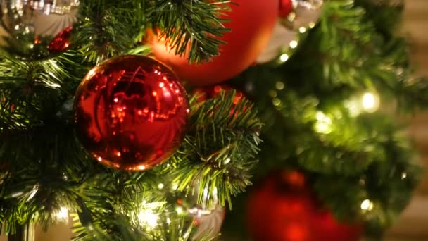 お祭り騒ぎの閉鎖ぼやけた輝く妖精の背景に明るい赤いボールを持つ屋外クリスマスツリー。ガーランドライトを使用しないと、ボケ効果。メリークリスマスとハッピーホリデーのコンセプト. — ストック動画