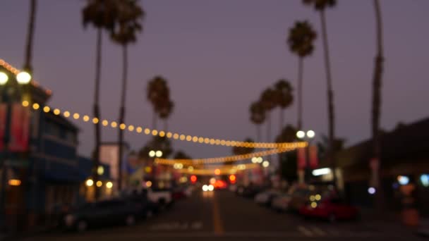 Dekoratif bakışlı çelenk ışıkları, palmiye ağaçları siluetleri, akşam gökyüzü. Bulanık arka plan. Kaliforniya 'da sokak lambalarıyla süslenmiş. Aydınlatma, plaj partisi, tropikal tatil konsepti.. — Stok video