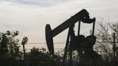 Endüstriyel şehir manzarası. La Brea Inglewood, Los Angeles 'ta. Çitin arkasında Jack 'i pompala. Sondaj kulesi ham petrol çıkarıyor. Çalışan pistonlu bir yağ makinası. Petrol ve doğalgaz endüstrisi