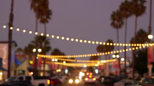 Decorativi fissando ghirlande luminose, sagome di palme, cielo serale. Sfondo sfocato. Strada decorata con lampade in California. Illuminazioni festive, festa in spiaggia, concetto di vacanze tropicali. — Video Stock