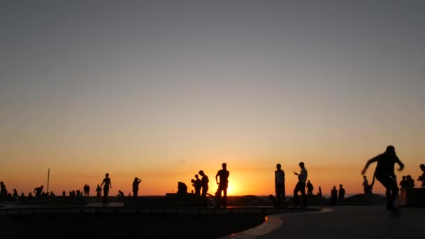 Silhouet van jonge springende skateboarder die longboard rijdt, zomer zonsondergang achtergrond. Venice Ocean Beach skatepark, Los Angeles Californië. Tieners op skateboard helling, extreem park. Groep tieners. — Stockvideo