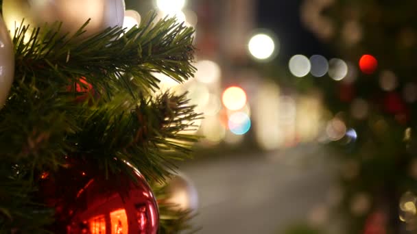 Primo piano di albero di Natale all'aperto festosamente decorato con palline rosso vivo su sfondo fata frizzante sfocato. Luci a ghirlanda sfocate, effetto Bokeh. Strada notturna sfocata con auto su strada — Video Stock