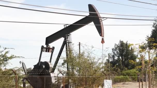 Průmyslová městská krajina. La Brea Inglewood v Los Angeles. No, pumpař operující za plotem. Těžba ropy z vrtné plošiny. Ropný důlní stroj s pístem. Odvětví ropy a zemního plynu — Stock video