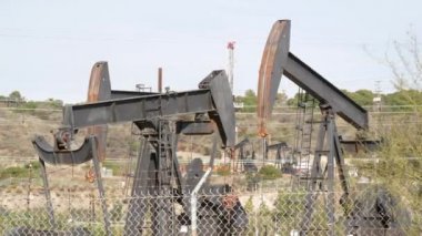 Endüstriyel şehir manzarası. La Brea Inglewood, Los Angeles 'ta. Çitin arkasında Jack 'i pompala. Sondaj kulesi ham petrol çıkarıyor. Çalışan pistonlu bir yağ makinası. Petrol ve doğalgaz endüstrisi