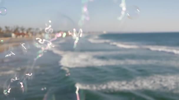 Soplando burbujas de jabón en el muelle del océano en California, fondo borroso de verano. Metáfora romántica creativa, concepto de soñar la felicidad y la magia. Símbolo abstracto de infancia, fantasía, libertad — Vídeo de stock