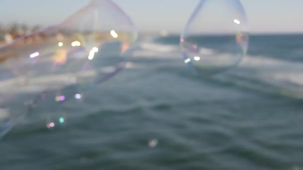 Blowing soap bubbles on ocean pier in California, blurred summertime background. Creative romantic metaphor, concept of dreaming happiness and magic. Abstract symbol of childhood, fantasy, freedom — Stock Video