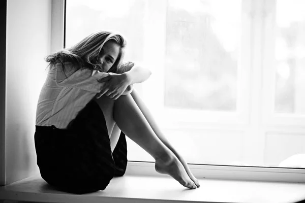 Jonge vrouw zittend op de vensterbank — Stockfoto