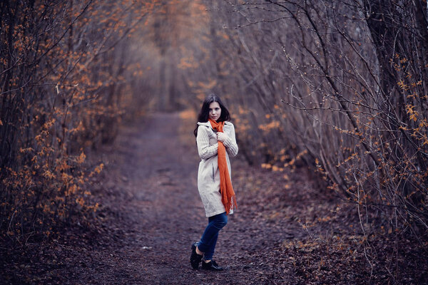 Young woman in a trench coat walks in autumn park