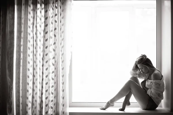 Ung kvinna sitter på fönsterbrädan — Stockfoto