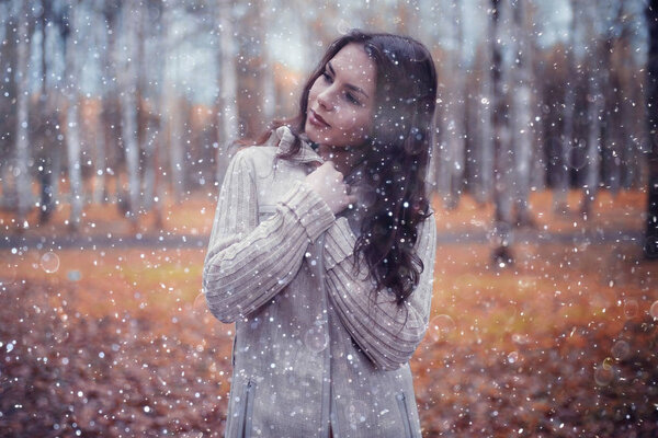 Portrait of young beautiful woman in park with snowflakes in the air