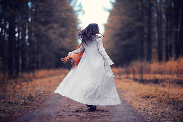 Young woman in white trench coat walking in autumn park