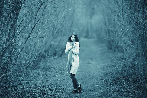 Young beautiful woman in white coat walking in autumn forest